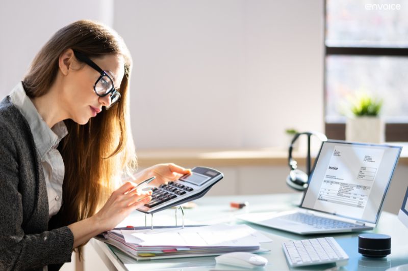 Woman using calculator and laptop with invoice screen, illustrating manual vs AP automation process.