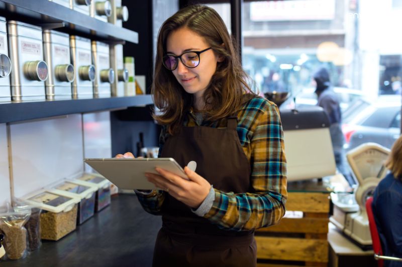 Small business owner using a tablet to manage finances, comparing QuickBooks Essentials vs Plus for bookkeeping needs