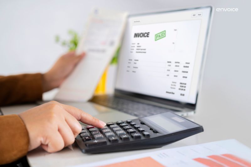 Automated invoice processing on a laptop screen with a 'Paid' status, as a person uses a calculator for financial tasks