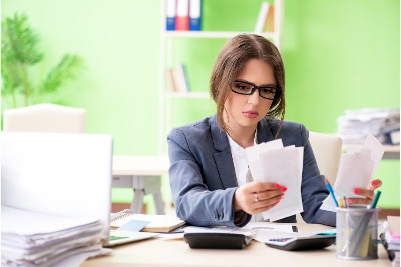 young woman stressed while holding paper invoices