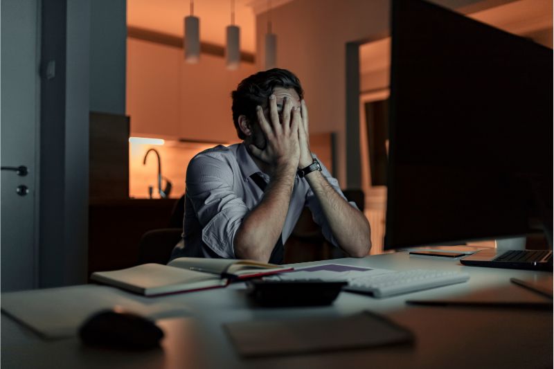 man exhausted covering his face in front of a computer