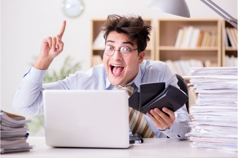 surprised man holding three calculators in front of a laptop