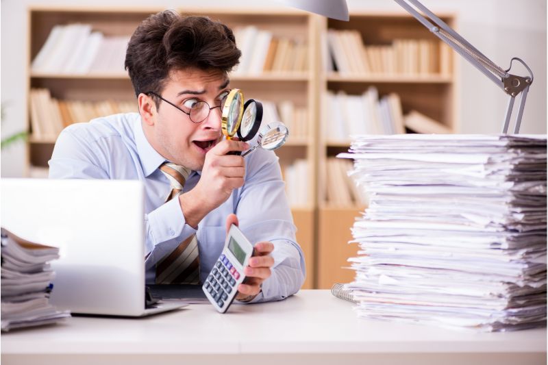 man using a magnifying glass; shocked of the stack of papers