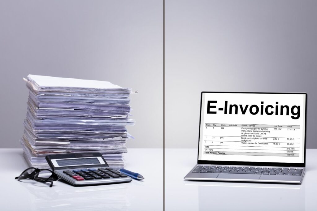 A stack of paper documents on the left side of the image is contrasted with a laptop displaying an electronic invoice on the right side.
