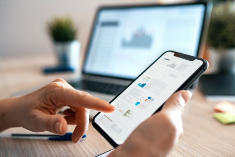 Person using a smartphone business expense tracker app with financial data visible on screen.